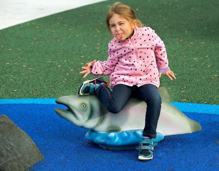 young girl sitting on salmon sculpture