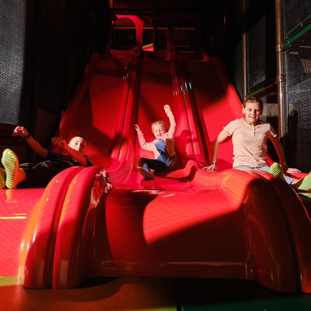 slides, three kids sliding down slides at an indoor playground